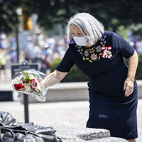 La gouverneure générale dépose des fleurs sur la Tombe du soldat inconnu. Nous y voyons des feuilles d'érable et un casque en bronze sculptés. Elle porte ses distinctions honorifiques canadiennes sur sa robe marine.