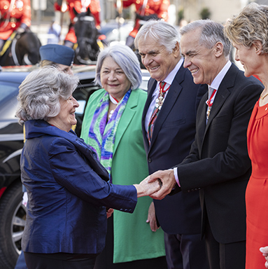 The Governor General Designate shaking hands with a row of dignitaries in front of a black car.