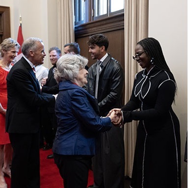 The Governor General shakes hands with a row of artists standing in a corridor. The Prime Minister and other dignitaries are also present.