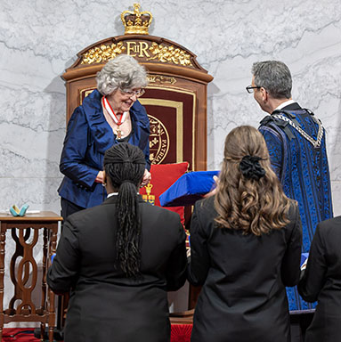 The Chief Herald of Canada, in ceremonial dress, presents a ceremonial collar on a velvet cushion for inspection by the Governor General.