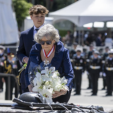 The Governor General places a bouquet of flowers on the Tomb of the Unknown Soldier. Two young men holding flowers stand on either side.