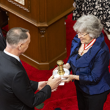 The Delegated Registrar General presents a large metallic disk surmounted by an ornamental handle to the Governor General.