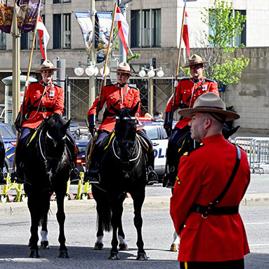 Four members of the Musical Ride of the Royal Canadian Mounted Police in ceremonial uniform. There is an officer standing in the foreground.