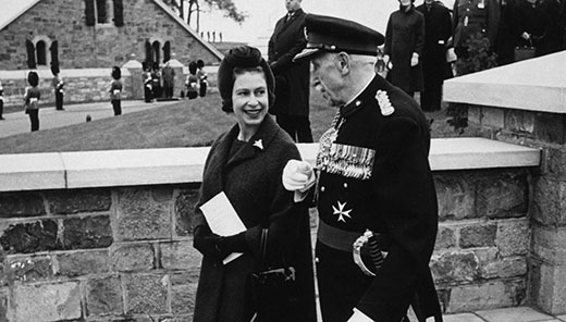 Photographie noir et blanc d'une jeune reine Elizabeth II marchant avec l’ancien gouverneur général Georges P. Vanier, en tenue militaire
