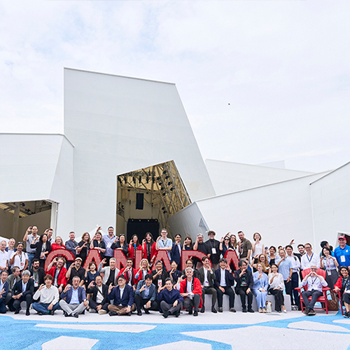 Un grand groupe de personnes posent devant une imposante structure blanche asymétrique.