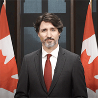 Le premier ministre Justin Trudeau prononce une allocution. Quatre drapeaux du Canada sont en arrière-plan.