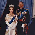 Sa Majesté la reine Elizabeth II et le duc d'Édimbourg, debout côte à côte, prennent la pose pour une photo officielle formelle à Rideau Hall. La Reine porte une longue robe blanche et dorée, tandis que le duc porte un uniforme militaire. Un drapeau canadien de cérémonie est visible à gauche en arrière-plan.