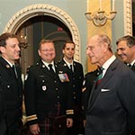 Le duc d'Édimbourg s'entretient avec des hommes en uniforme des Forces armées canadiennes. Ils sont tous debout. 