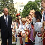 The Duke of Edinburgh walking outside next to a lineup of young boys and girls dressed in traditional costumes.