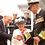 The Duke of Edinburgh shaking hands with a man aboard a Canadian navy ship. Her Majesty Queen Elizabeth II is standing in close proximity and smiling.
