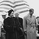 Princess Elizabeth and Prince Philip walk down a path between two rows of Indigenous community members dressed in full regalia.