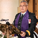 Un homme en tenue militaire portant une étole violette parle à un lutrin.