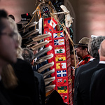 2 Eagle Staffs, with visible Indigenous and national symbols, are seen through a crowd of people.