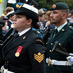 Members of a parade wearing military attire and decorations march along a street.