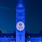 Un édifice de la capitale est illuminé la nuit en bleu royal, avec le monogramme de la Reine projeté au centre.