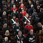 An aerial view of people in military and RCMP attire marching down the nave of a church, observed by audience members standing in pews.