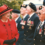 Queen Elizabeth II smiling to veterans in a receiving line, outside.
