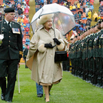 Queen Elizabeth II walking outside, with an umbrella, in front of a guard of honour.