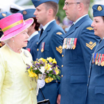 Queen Elizabeth II, holding flowers, walks in front of members of the Canadian Armed Forces.