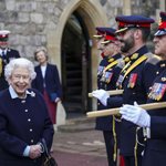 Qeen Elizabeth II, dressed in a dark suit, smiles while meeting Canadian military personnel lined up in front of her.