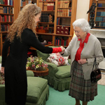Queen Elizabeth II and Governor General Julie Payette are standing in front of a fireplace. They are shaking hands and smiling.