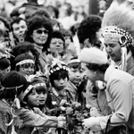 Black and white image of Queen Elizabeth II accepting a bouquet offered by a child. Chief Wellington Staats stands beside her.