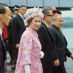 Queen Elizabeth II walking outside with men in suits.