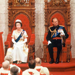 The Queen and the Duke of Edinburgh, seated on the Senate thrones. She is wearing a white gown and tiara. He is wearing a military uniform.