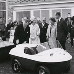 Queen Elizabeth II, the Duke of Edinburgh and Prime Minister Lester B. Pearson are gathered in front of a small cart.