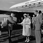 Black and white image of the Queen shaking hands with Inspector E. Porter after getting off the plane. The Duke of Edinburgh is by her side.