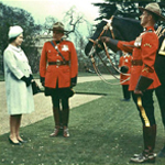 Queen Elizabeth II looking at a black horse presented to her by two members of the RCMP.