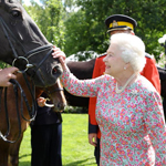 Queen Elizabeth II, outside, petting the head of an RCMP horse.