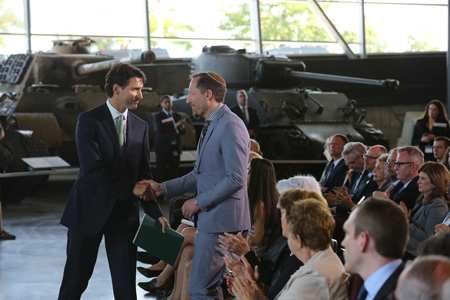 Prime Minister Justin Trudeau greeting a man, in front of an audience of people at the Canadian War Museum in Ottawa.