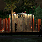 Visitors are shown on a viewing platform atop a cube structure made of perforated metal which is shown illuminated at night.
