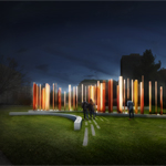 Visitors approach clusters of slender bronze columns illuminated at night