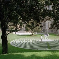 A person is outside, walking through a stone labyrinth set in a grassy lawn.