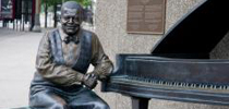 Photo of a bronze statue of Oscar Peterson seated on a bench beside his piano.