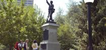 Photo d’une statue de bronze représentant un soldat en uniforme qui, d’un côté, tient son fusil et, de l’autre, soulève son chapeau en saluant.