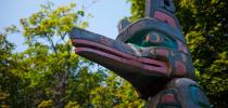 Photo of the head of the Kwakiutl totem pole with trees in the background.