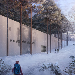 A person is walking along a pathway that is covered in snow.  A large concrete wall has a face etched on it with the words “who, what, when, why”. It is surrounded by landscaping and tall pine trees that are covered with snow.