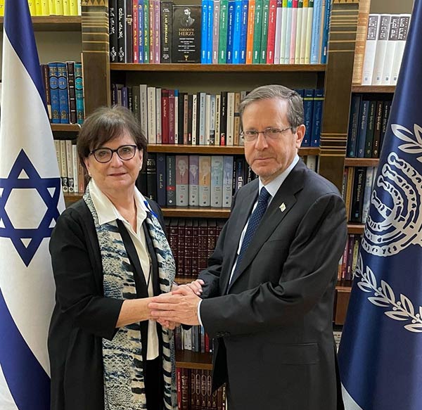 Deborah Lyons tenant les mains du président israélien Isaac Herzog devant une bibliothèque, avec deux drapeaux israéliens en arrière-plan