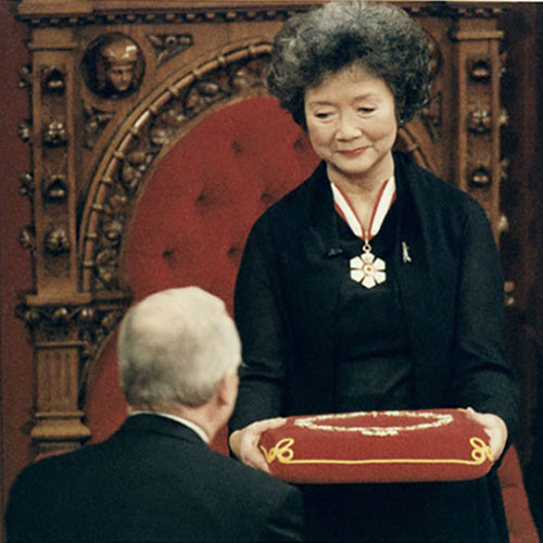 Adrienne Clarkson is holding a decorative pillow upon which rests a ceremonial collar.