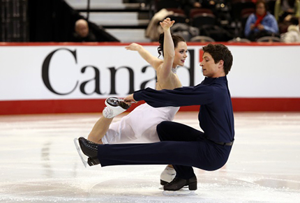 Deux patineurs avec le mot-symbole Canada qui apparaît en arrière-plan sur la bande de la patinoire.