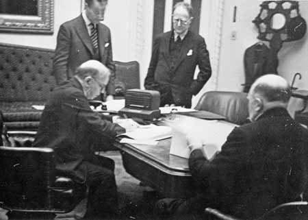 O.D. Skelton observes a signing ceremony by Prime Minister William Lyon Mackenzie King.