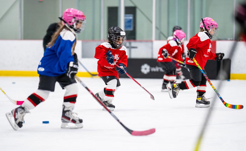 Children playing hockey on an indoor rink.