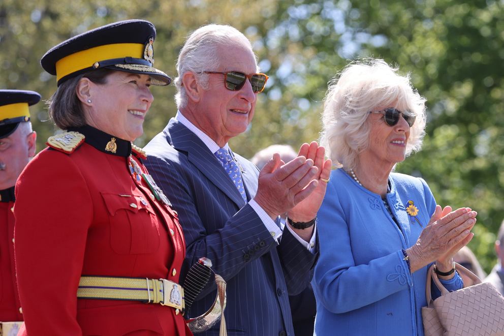 The Prince of Wales and the Duchess of Cornwall clapping, while standing next to the RCMP Commissioner Brenda Lucki.