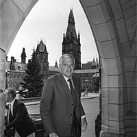 John Turner walks and smiles as he walks through an archway on Parliament Hill.