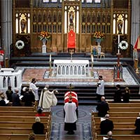 A view of the interior of the cathedral. The casket, covered with the National Flag of Canada, can be seen in the central aisle, surrounded by clergy members and guests.