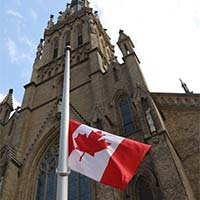 Le drapeau national du Canada flotte en berne. À l’arrière-plan, une flèche de pierre de la basilique-cathédrale St. Michael.