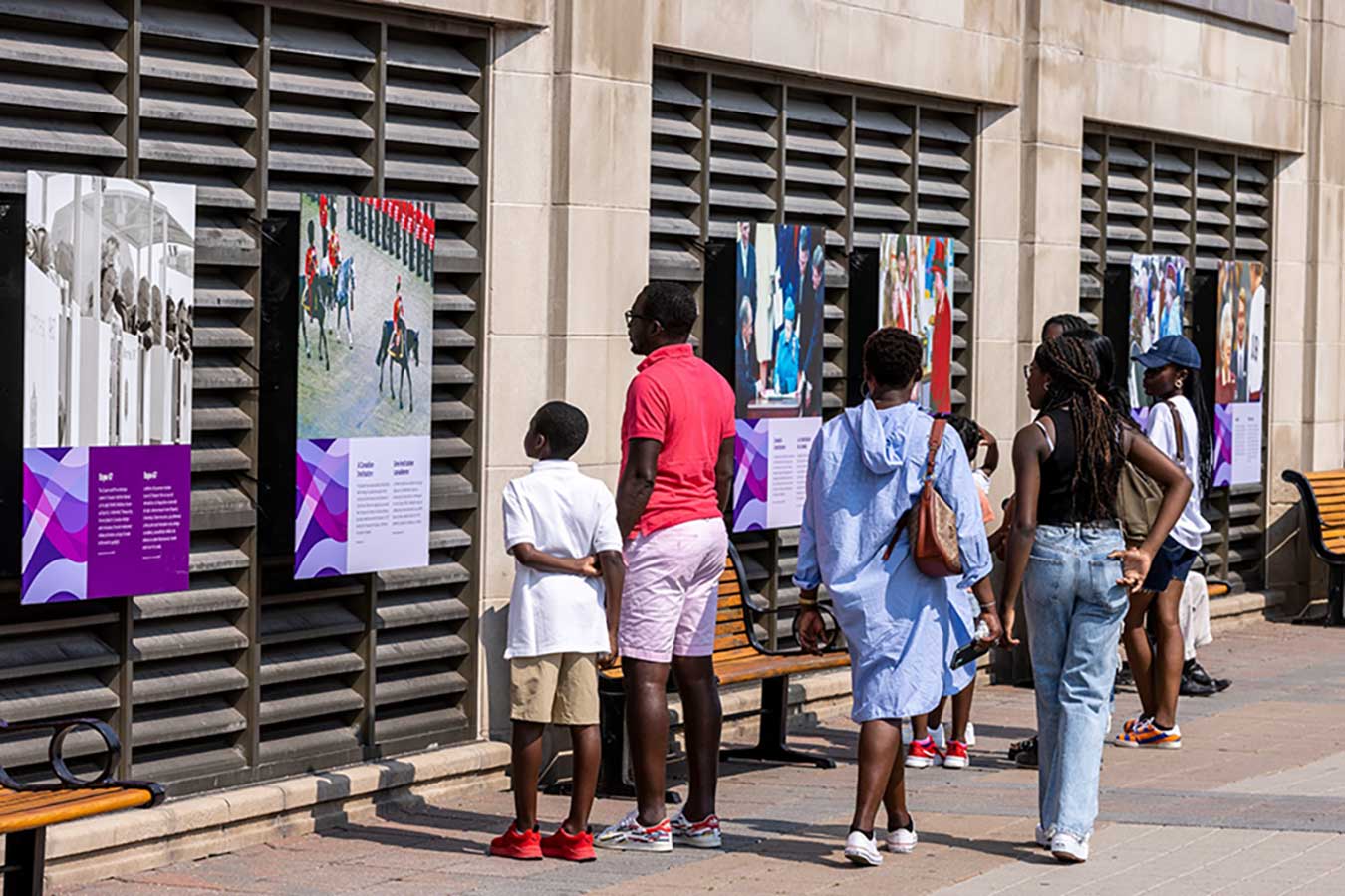 Des gens marchent et s'arrêtent en regardant une exposition extérieure composée de panneaux avec des photos et des textes.